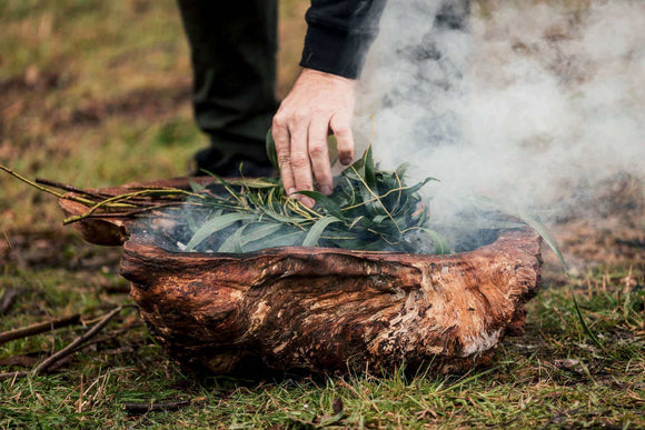Photo of a person adding foulage to a fire for a smoking ceremony.